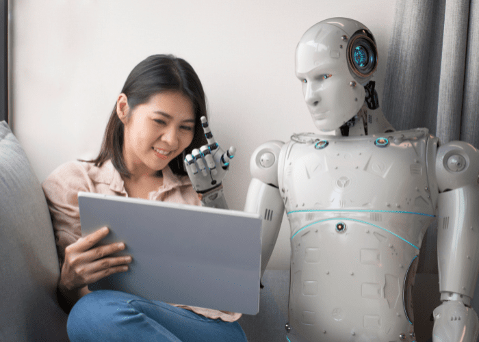 Robot sitting beside woman with laptop